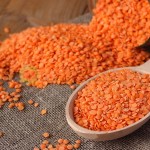 Refined red lentils in wooden spoon and glass jar on linen sackcloth